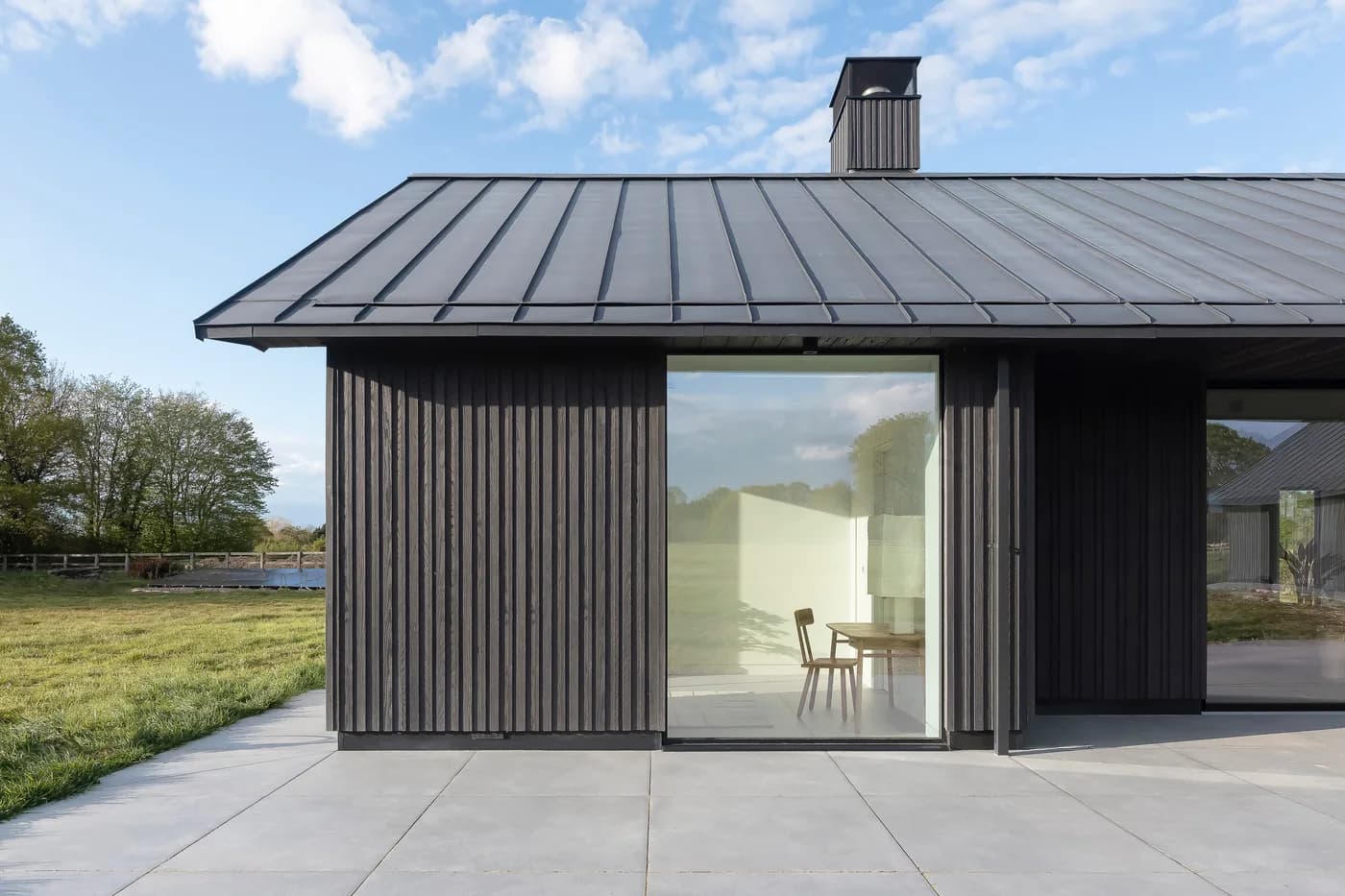 Full-height picture window in a dark timber-clad elevation beside a lawn