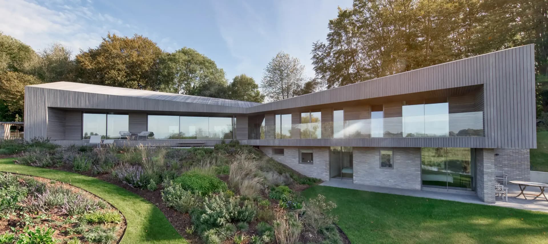 Slim-framed Maxlight glazing — a long uninterrupted glass elevation wrapping a contemporary timber-clad house above a brick base