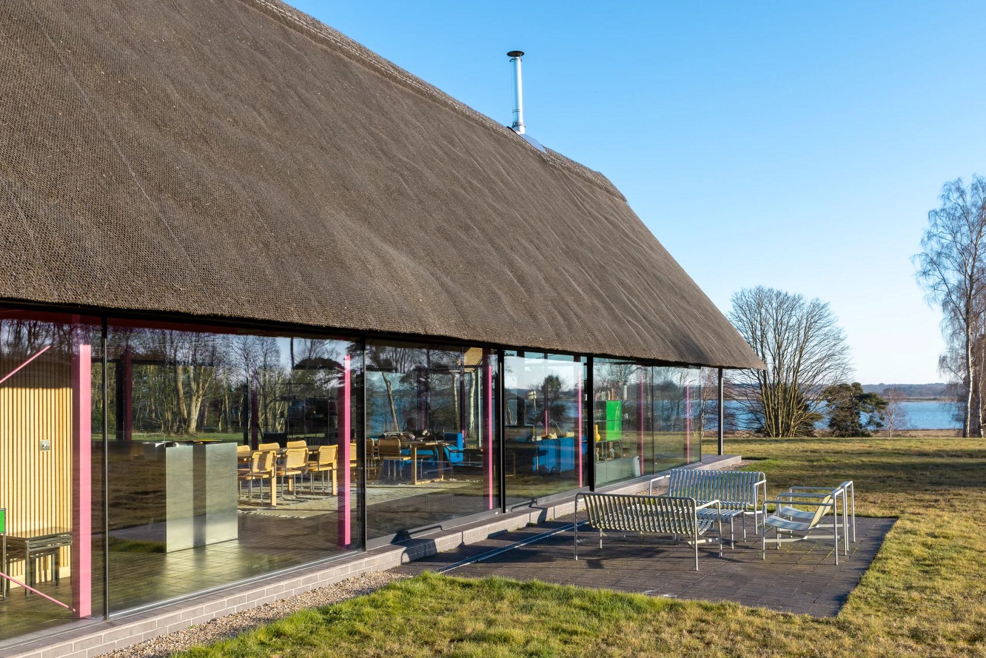 Housestead: a single-storey thatched home wrapped in a full-height Maxlight glass envelope on a slender steel frame, overlooking the River Alde under winter light.