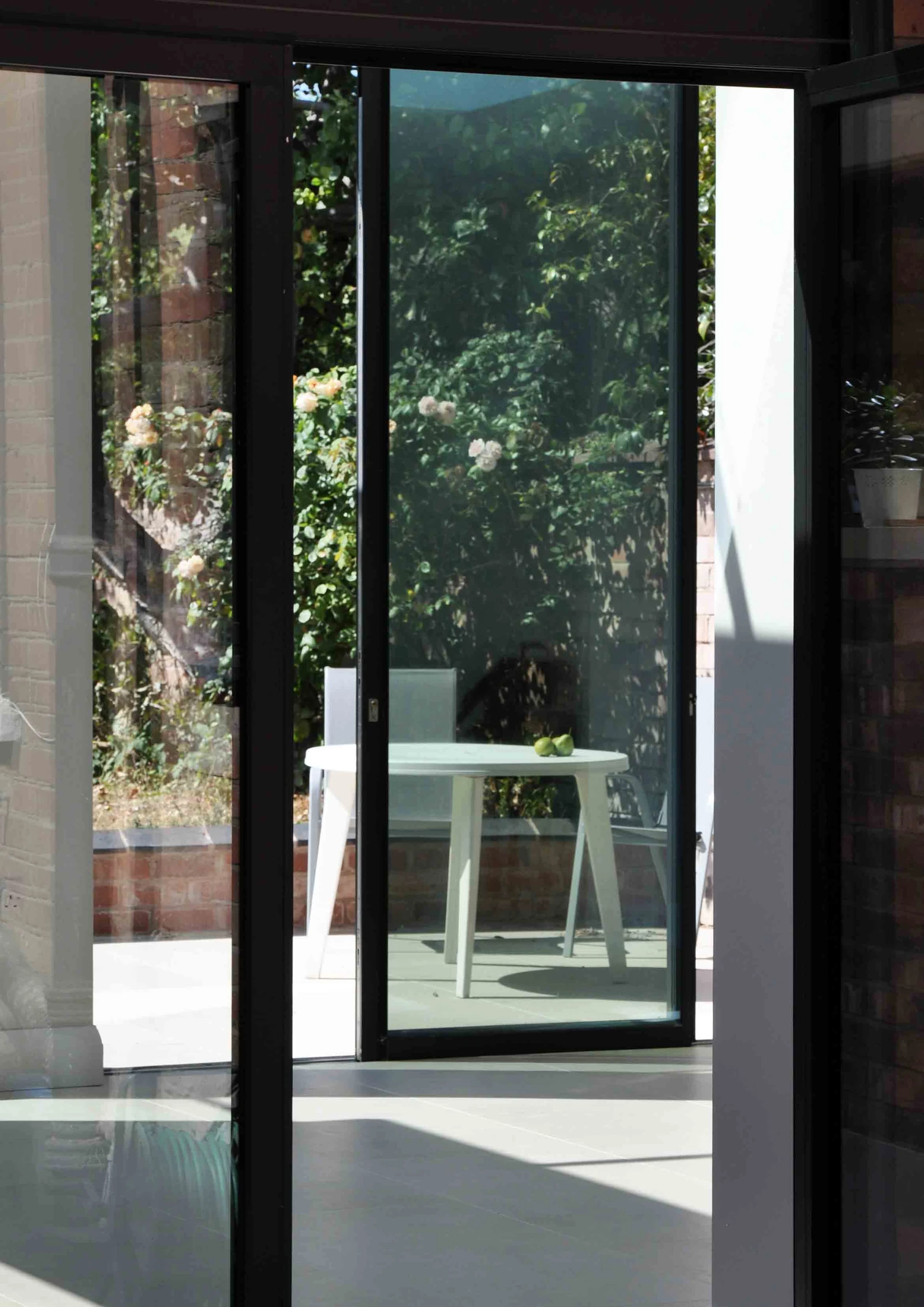 View through slim dark glazing frames towards a round table on the garden terrace.