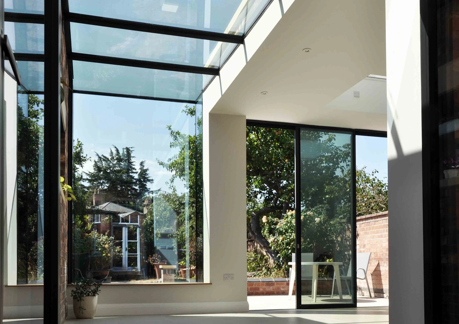 Interior beneath the glass roof, with sky views above the glazed bay and sliding doors towards the garden.