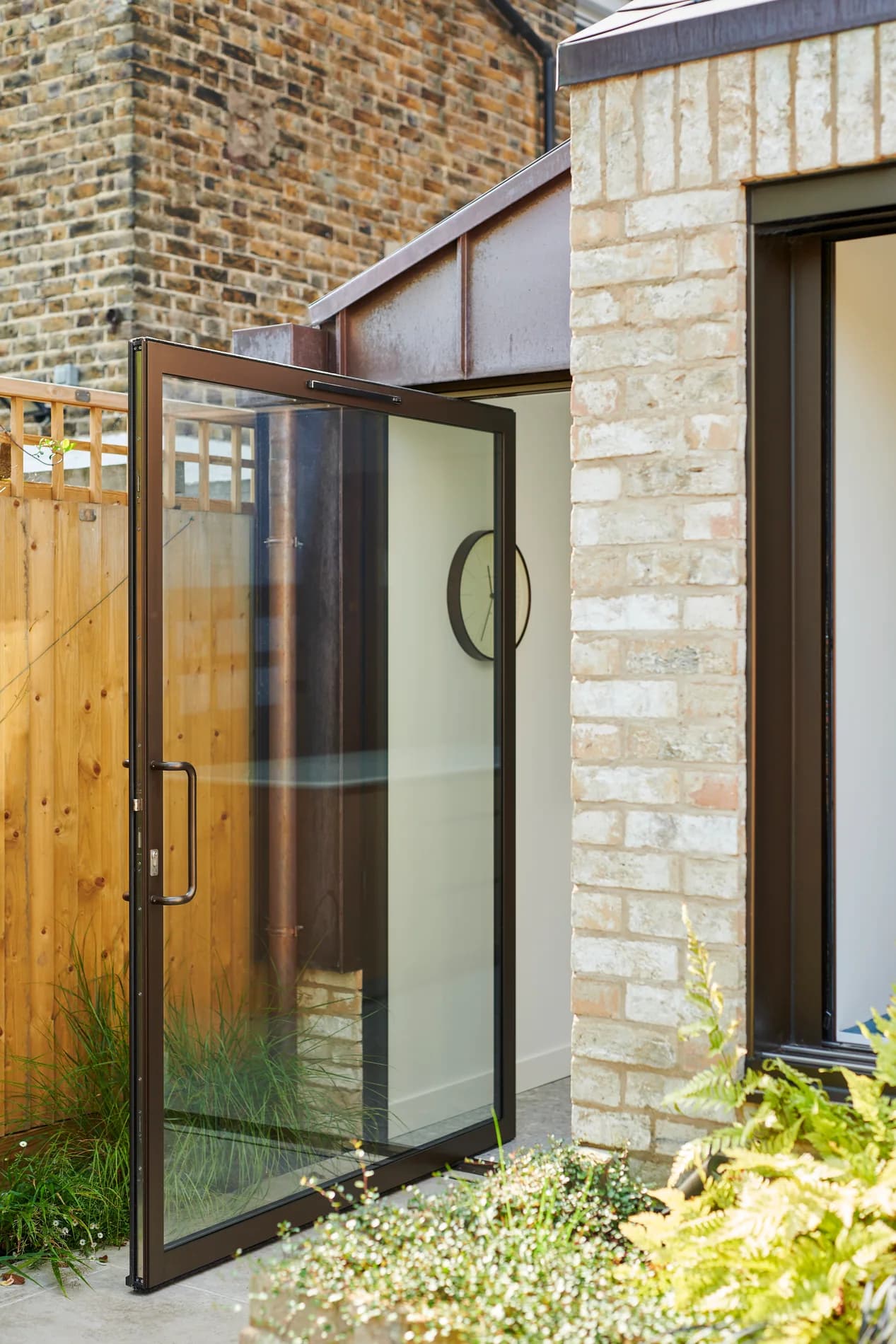 F-Max aluminium pivot door open beside a brick residential entrance