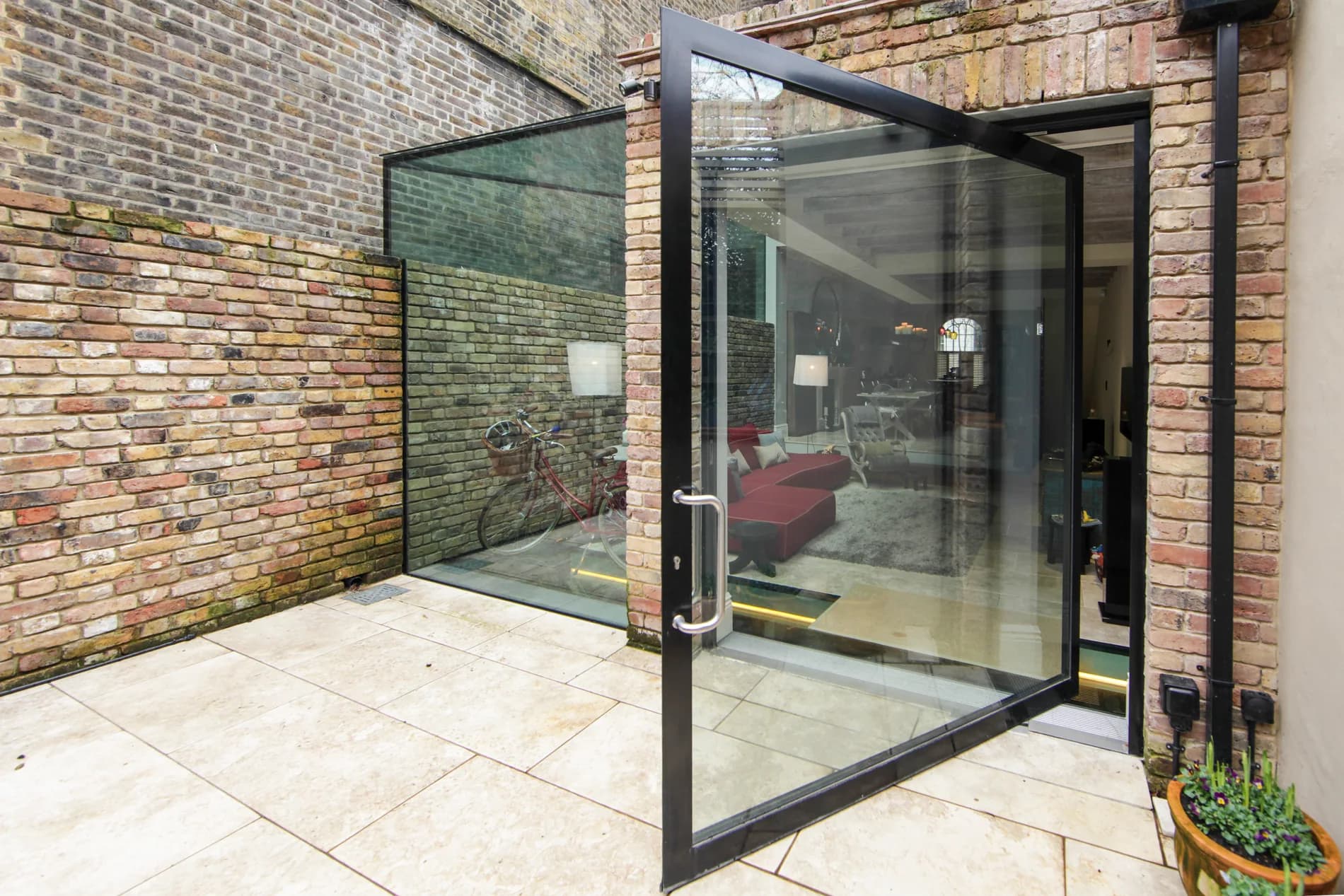 X-Max steel-inspired pivot door open across a brick courtyard threshold