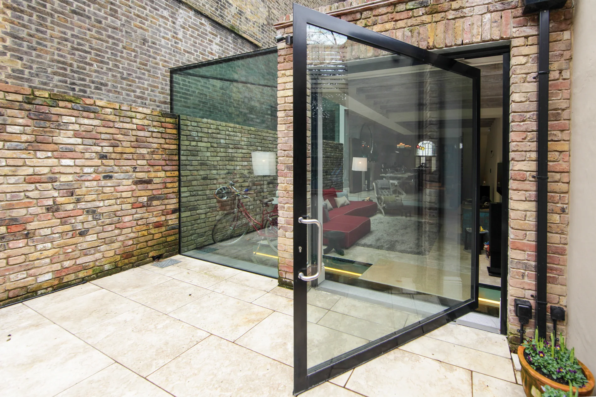 X-Max steel-inspired pivot door open across a brick courtyard threshold