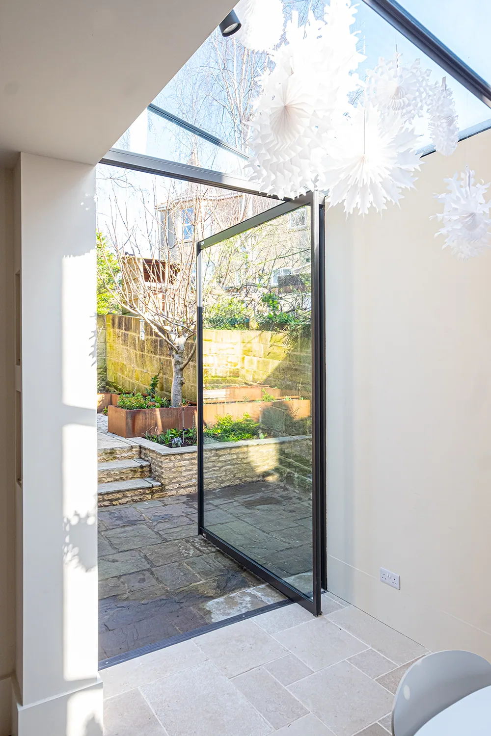 F-Max pivot door opening from a light interior to a paved garden