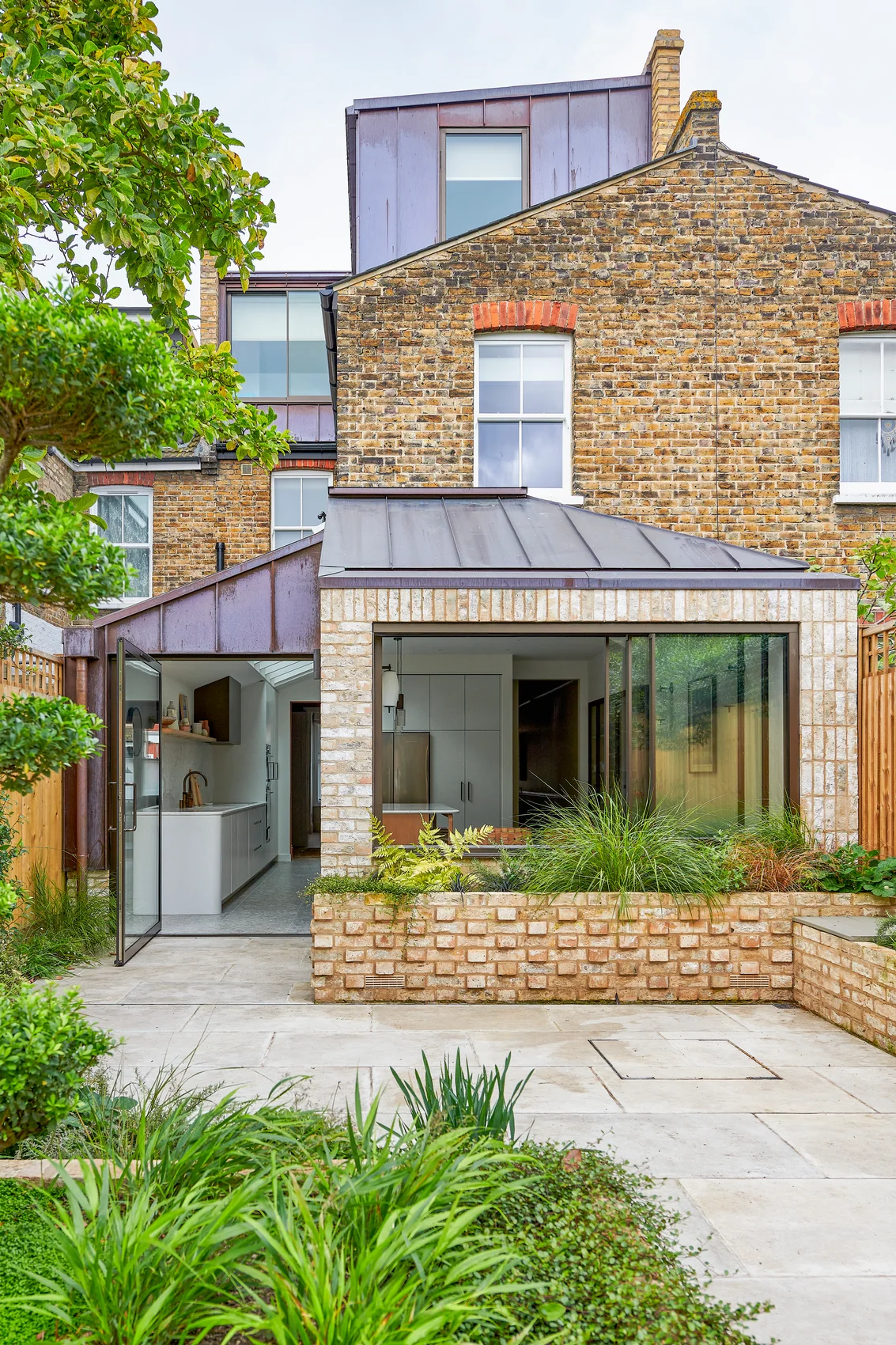 Framed pivot door on a brick rear elevation with garden planting