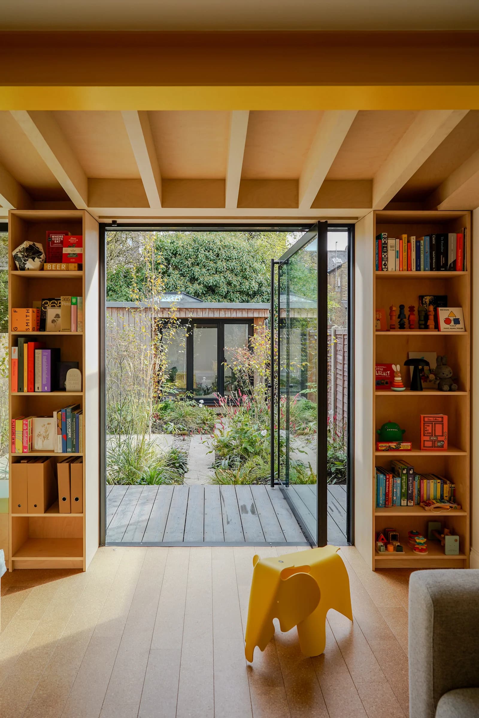 Full-height aluminium pivot door opening from a timber-lined room towards a garden