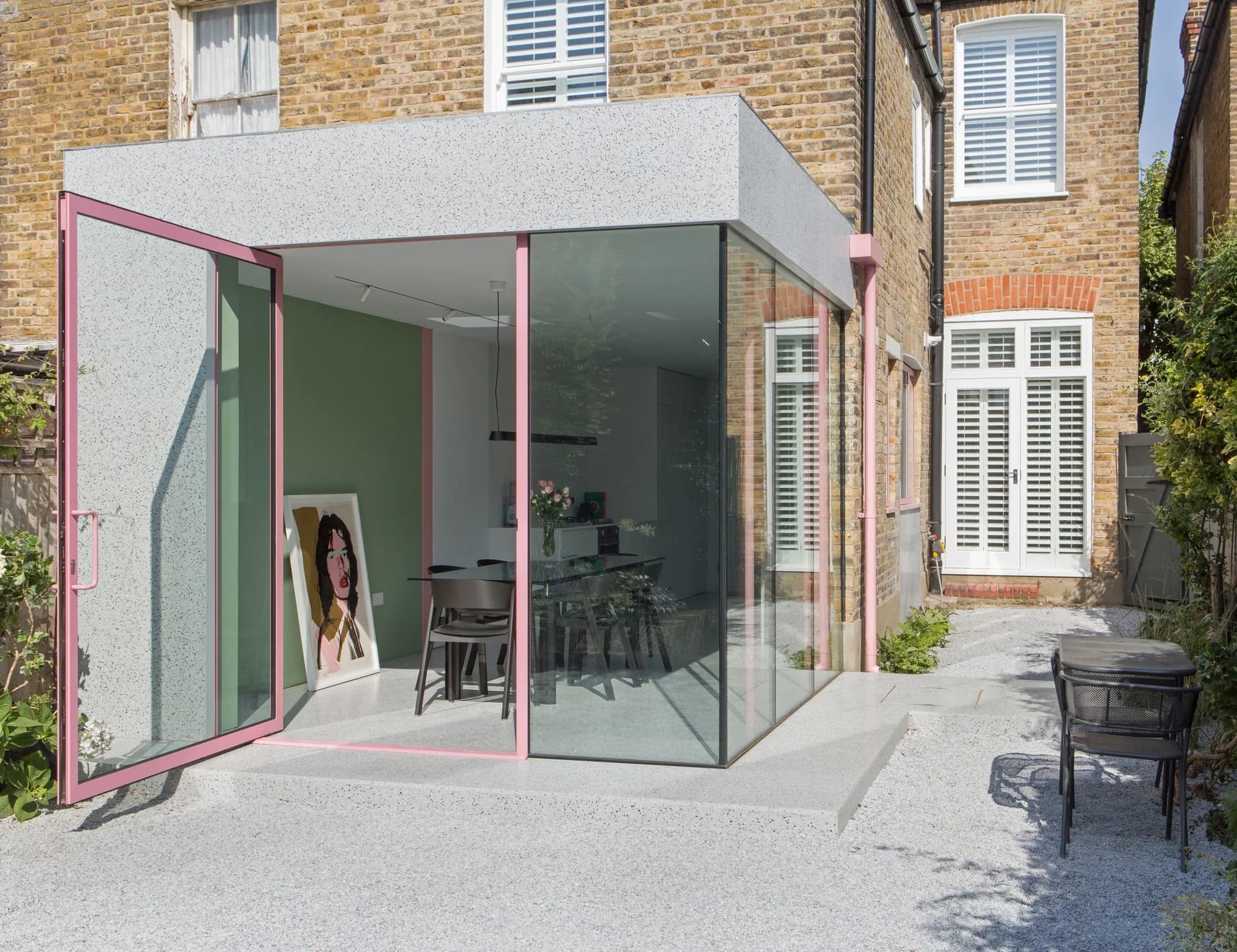 Pink-framed Maxlight pivot door open beside structural glazing on a contemporary rear extension