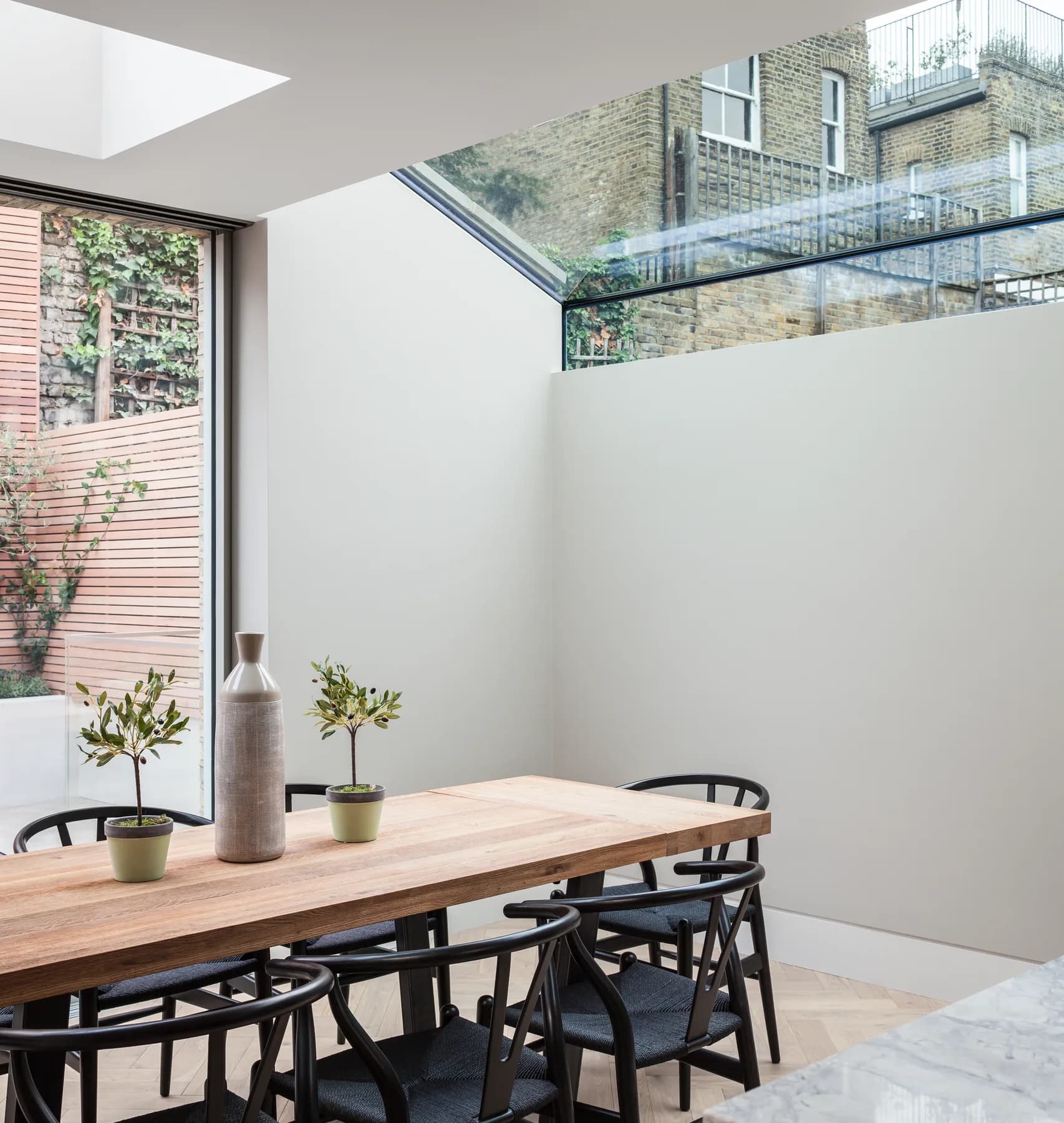 Dining table below a tall up-and-over rooflight beside a courtyard wall