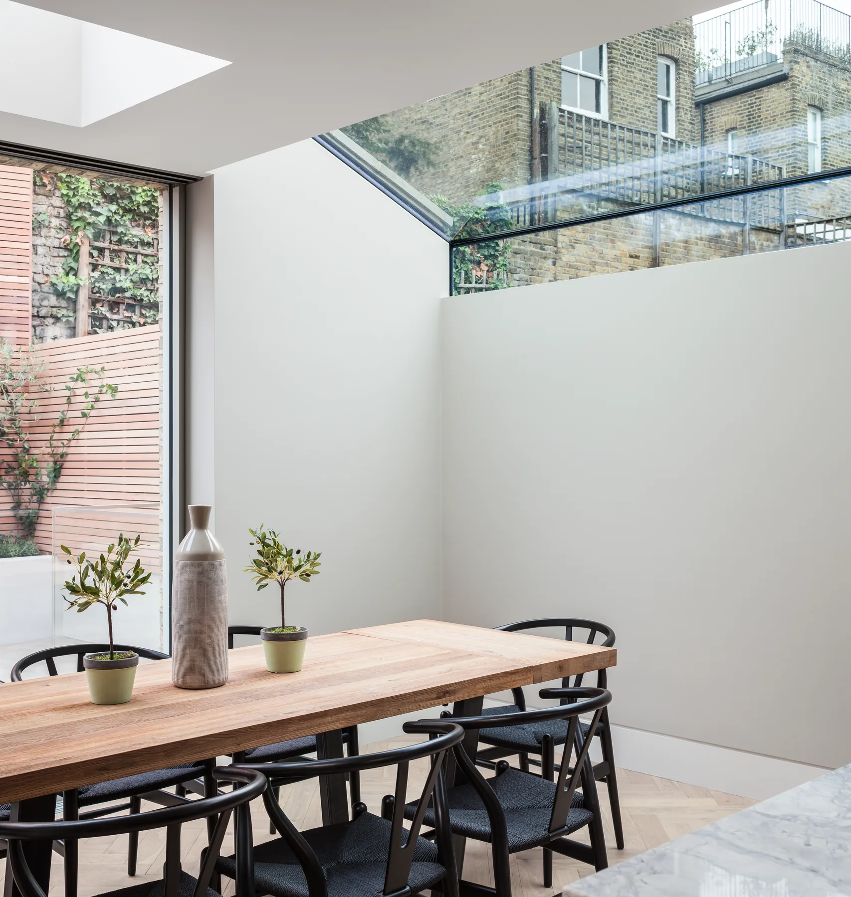 Dining table below a tall up-and-over rooflight beside a courtyard wall