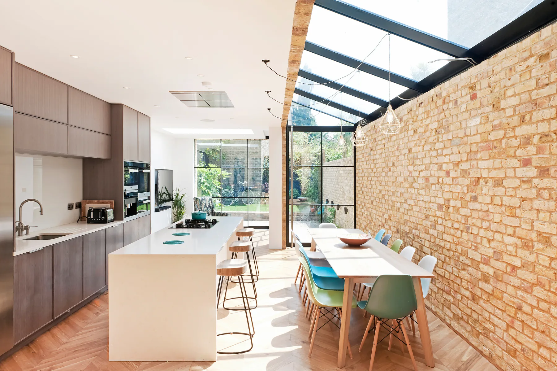 Open kitchen and dining space below a glazed roof against an exposed brick wall