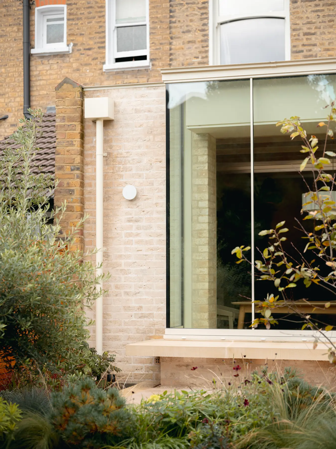 Glass-to-glass corner structural glazing detail beside brickwork and planting