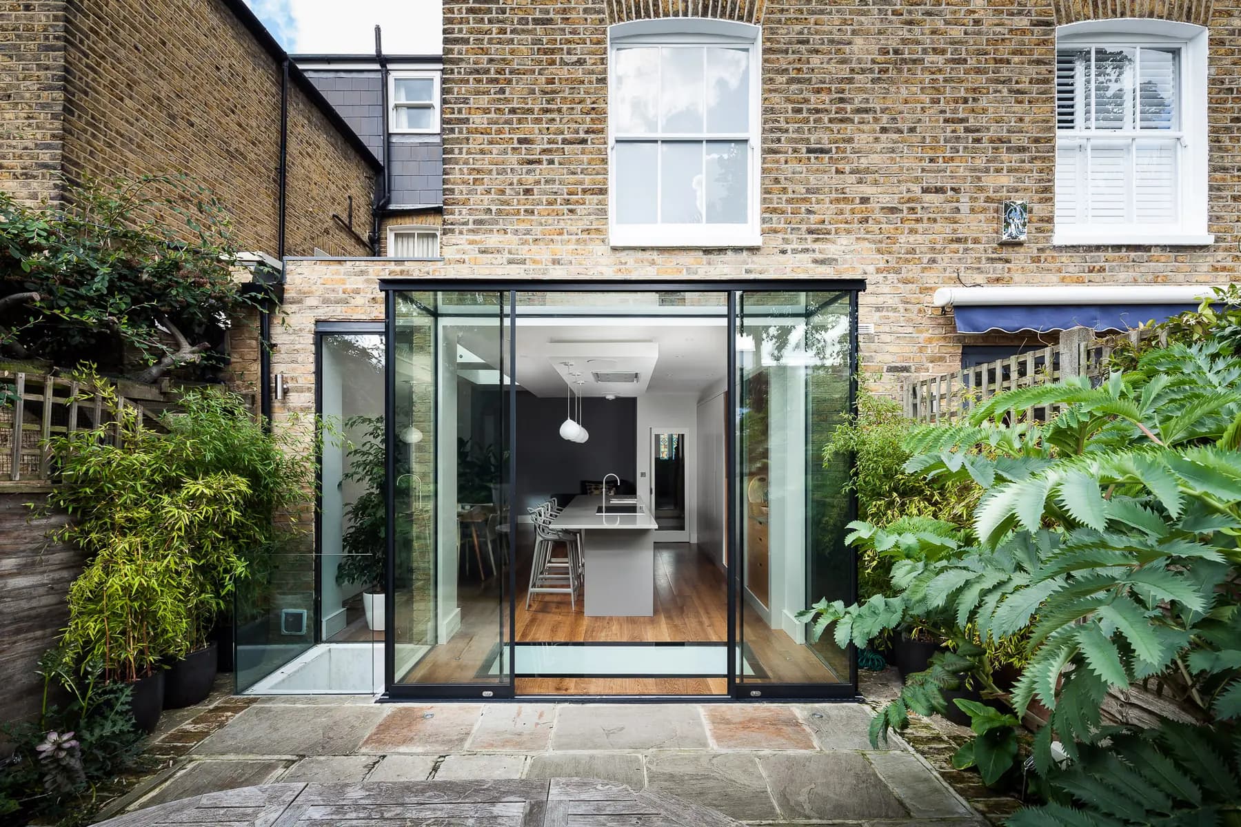 Glass box extension opening from kitchen to a paved garden terrace