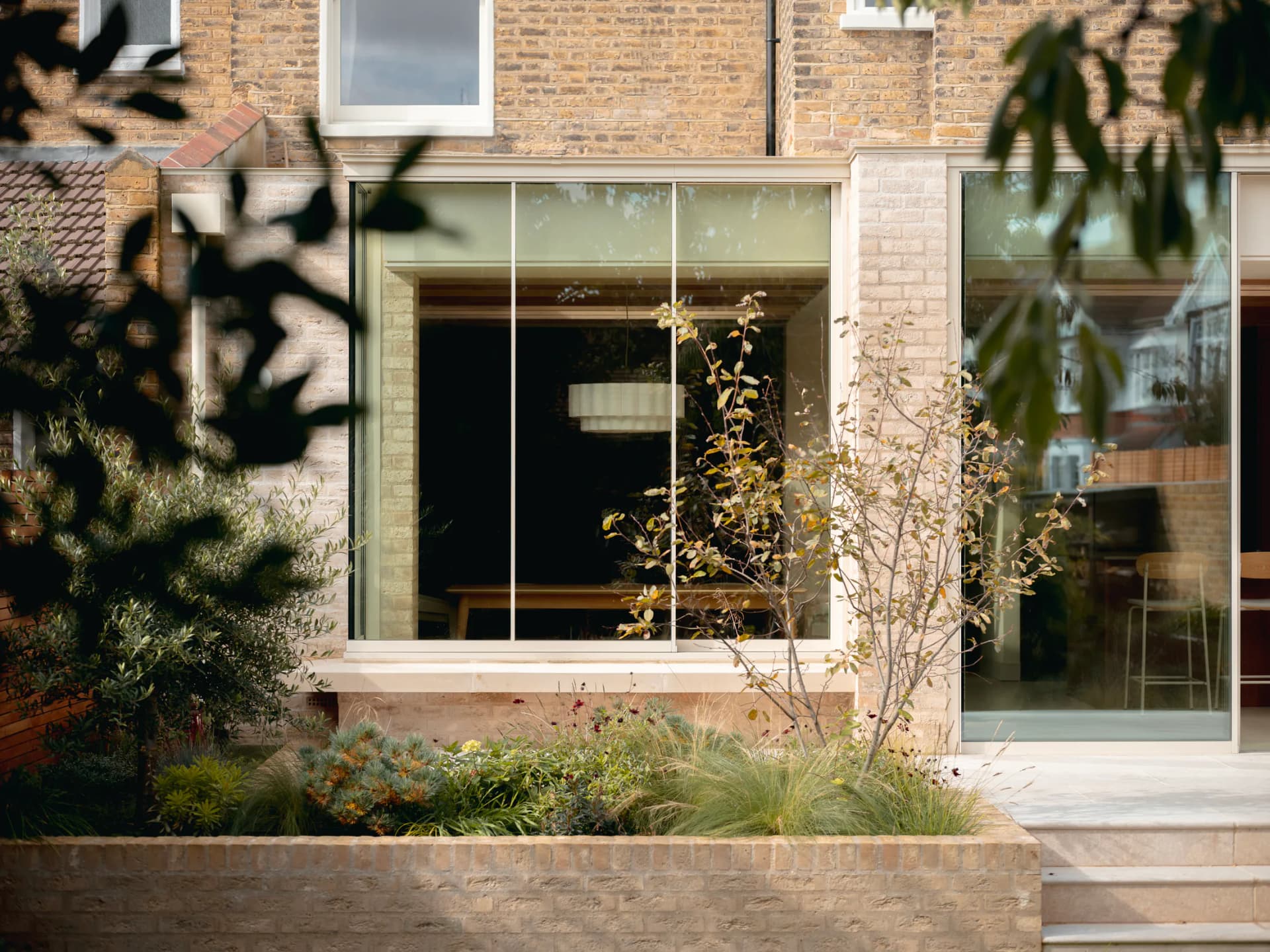 Slim aluminium sliding window set into a brick residential extension with garden planting