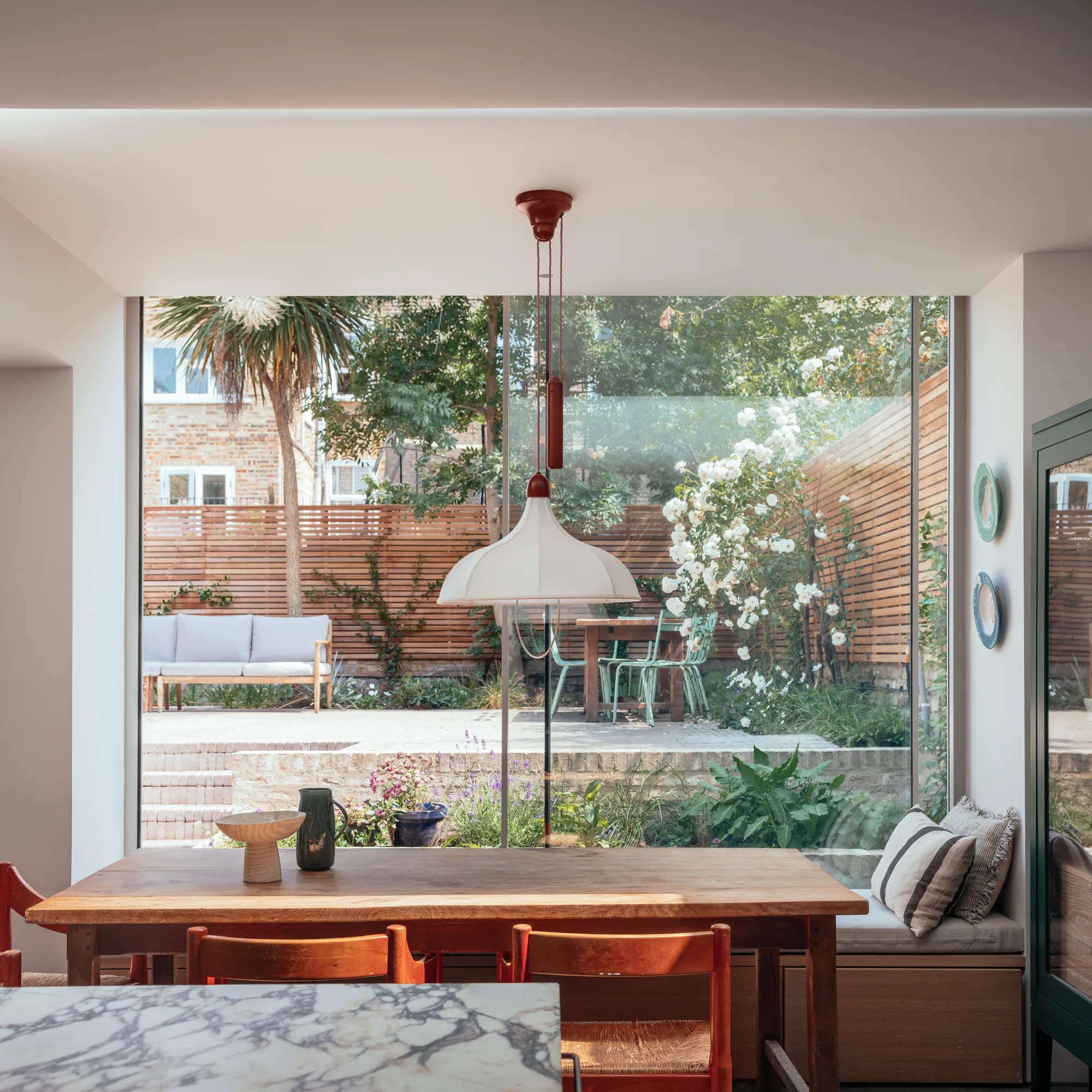 Full-width aluminium sliding window framing garden planting from a dining room