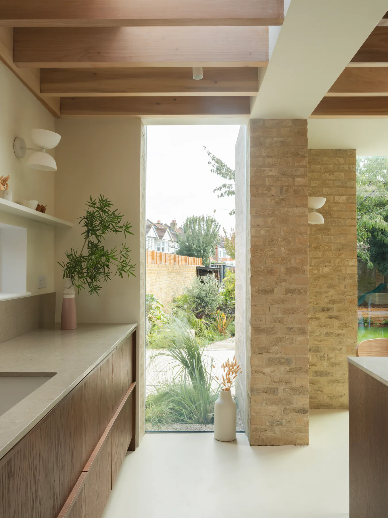 Tall fixed window drawing garden light into a brick and timber kitchen