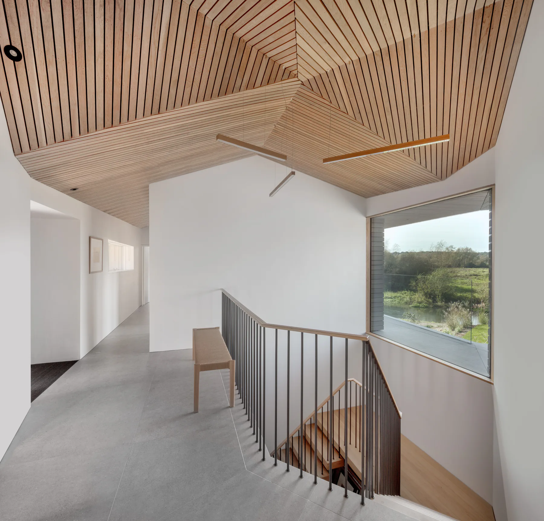 Panoramic fixed window wrapping the landing of a timber-lined stair hall