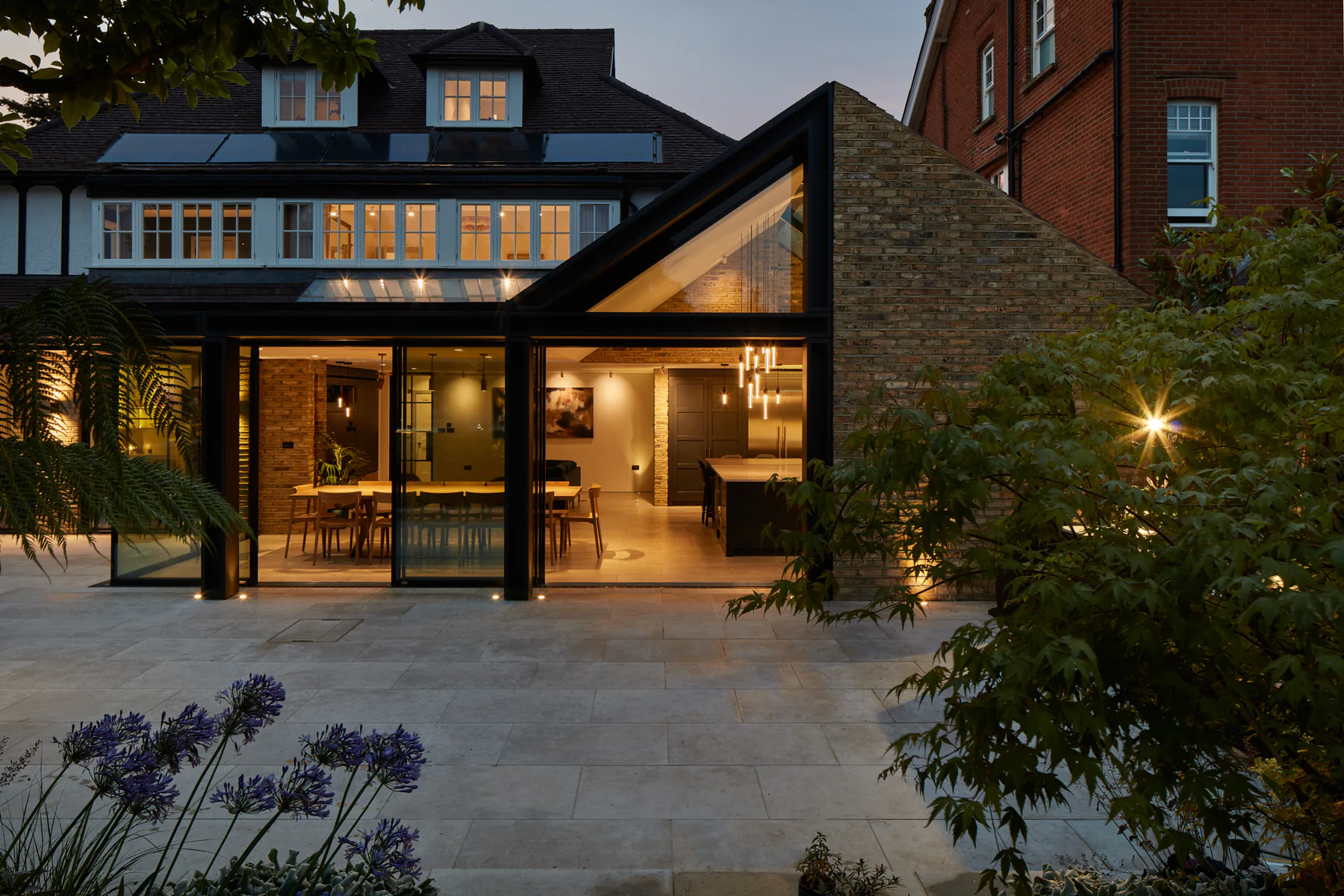 Fixed glazing and a triangular gable window illuminating a garden extension at dusk