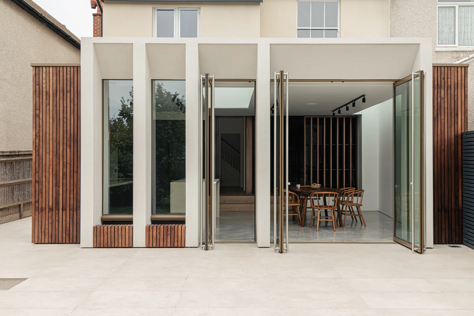 Tall fixed sidelights arranged around a glazed pivot door on a timber-clad facade