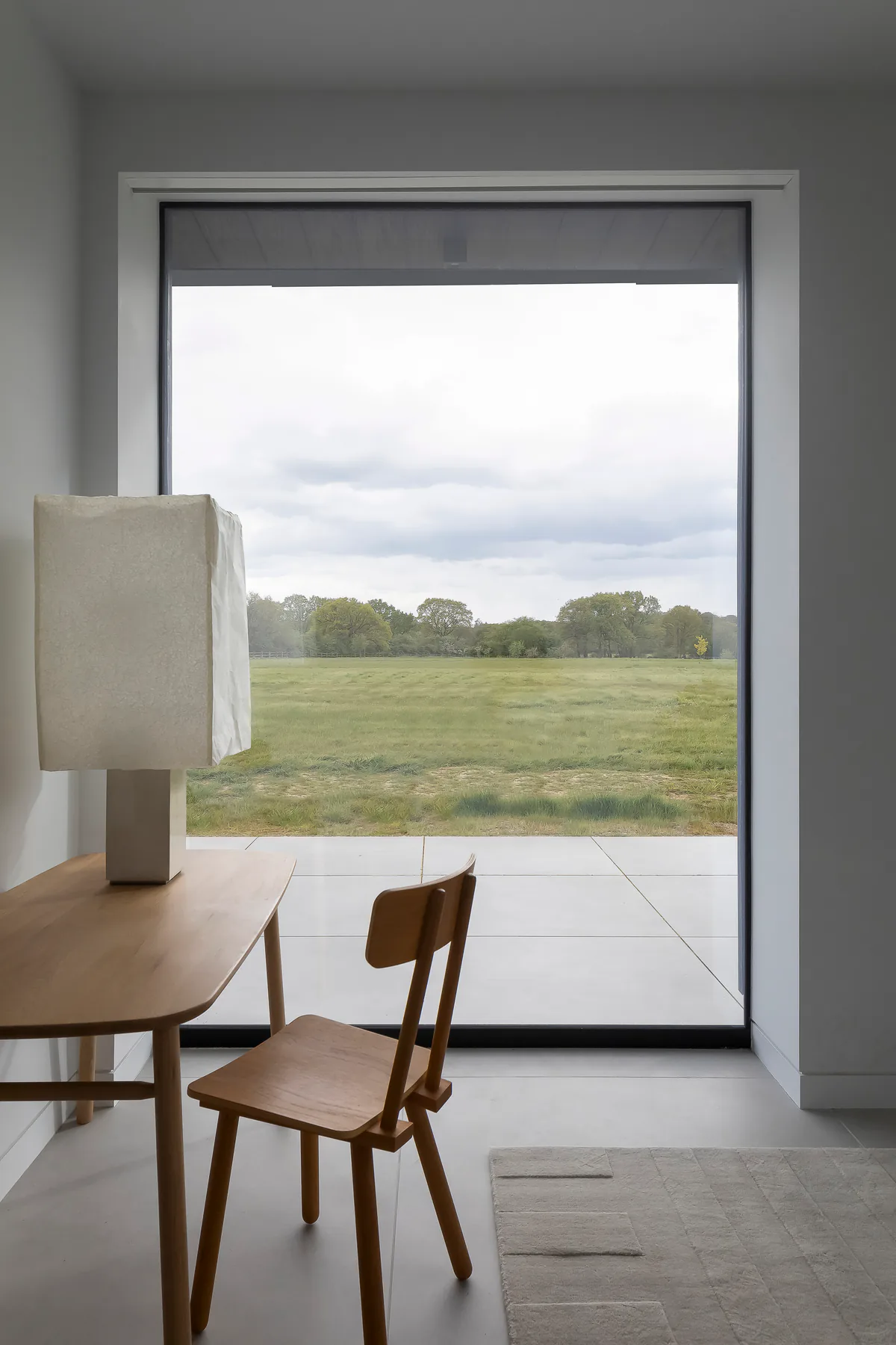 Full-height fixed window framing a wide rural landscape from a dining room