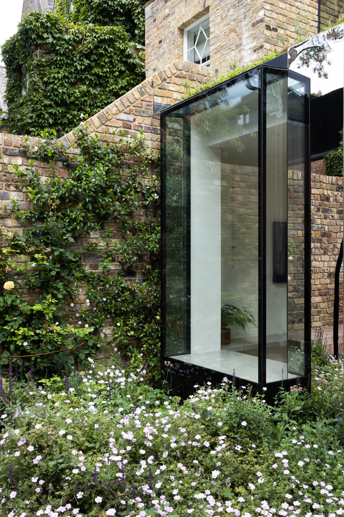 Glass oriel bay window projecting from a brick home above garden planting