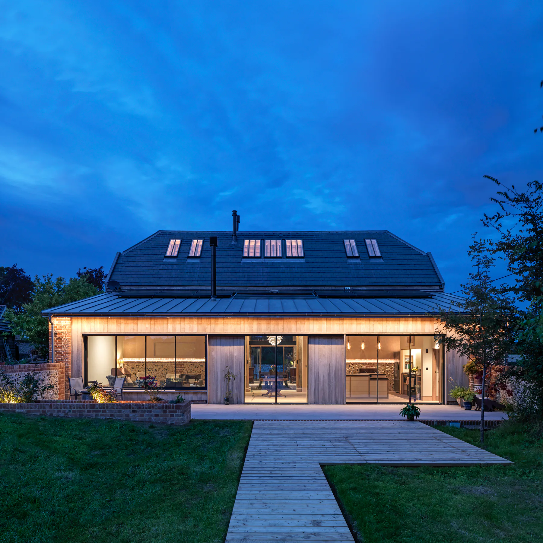 Wide sliding window illuminating a barn extension at blue hour