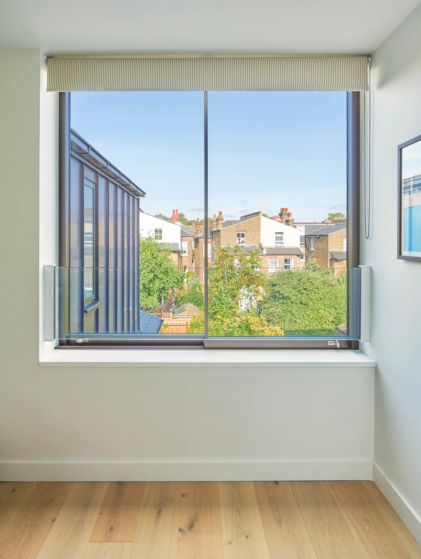 Slim aluminium sliding window framing rooftops from a white interior