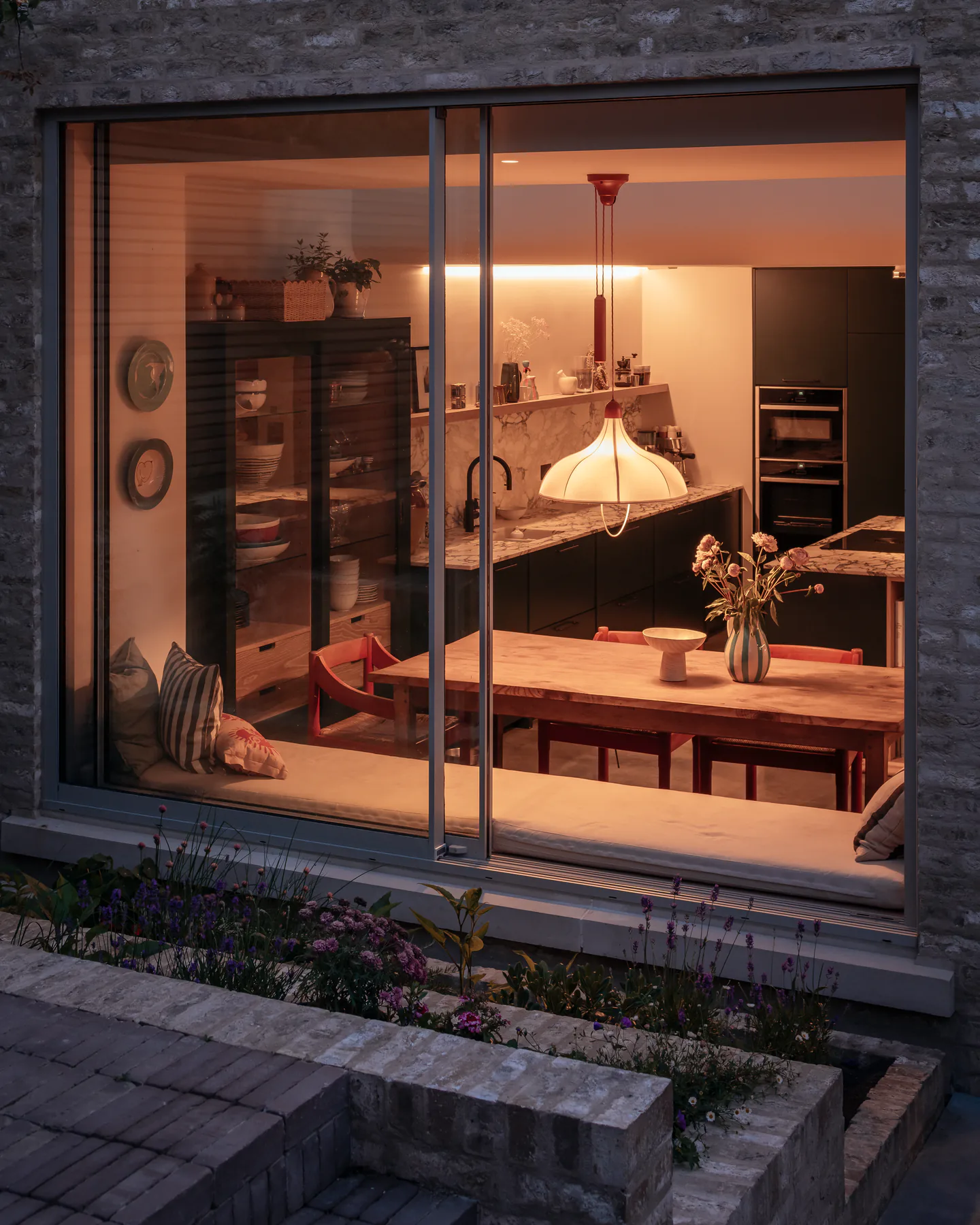 Dining room seen through a slim sliding window on an evening exterior